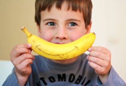 Little boy smiles with a banana over his mouth
