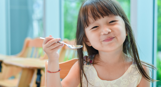Little girl smiles and holds up a spoon